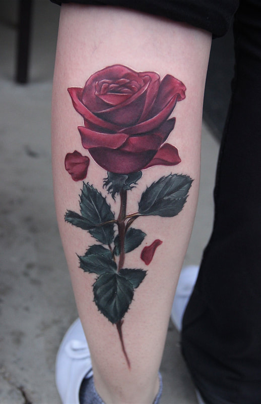 Color realism red rose tattoo with green leaves down a woman's forearm.