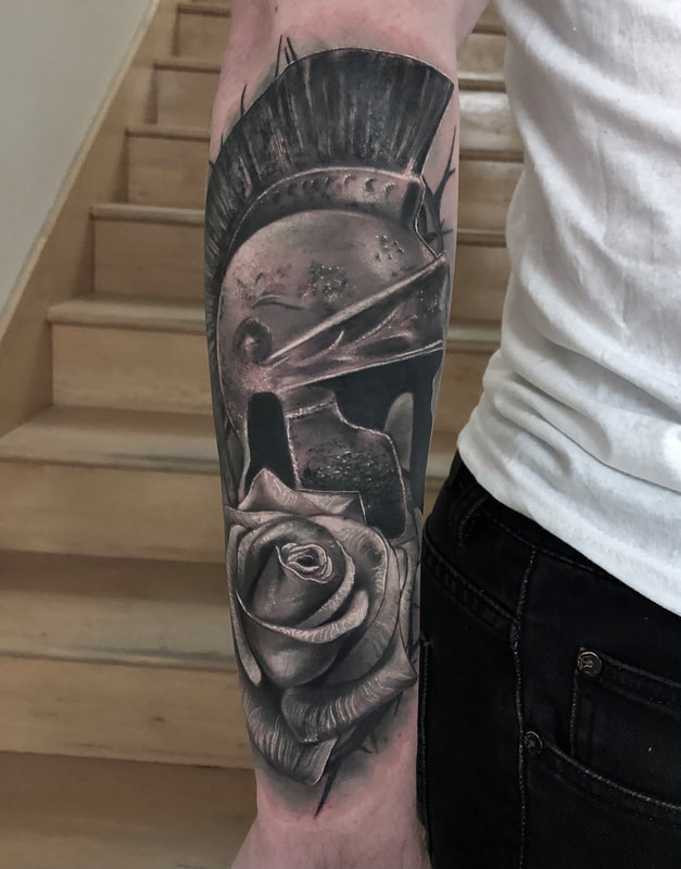 Realistic black and gray Spartan helmet and rose tattoo on a forearm.