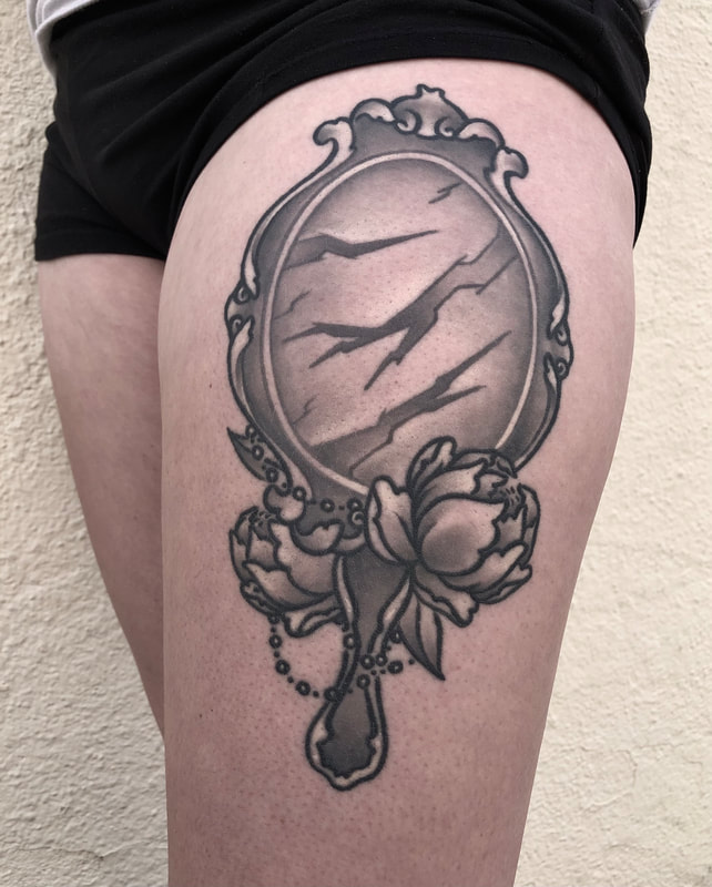 Black and grey realistic tattoo of the mirror from the movie Beauty and the Beast on a thigh.