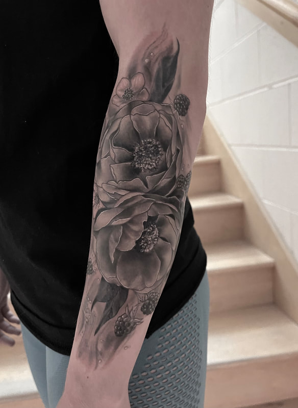 Black and grey realistic tattoo of flowers on a forearm.