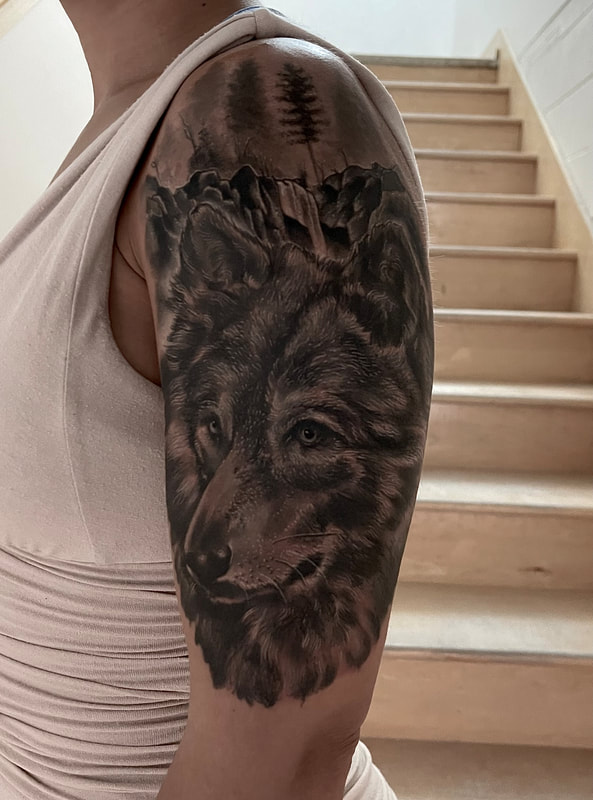 Realistic black and grey tattoo of a wolf head on an upper arm.