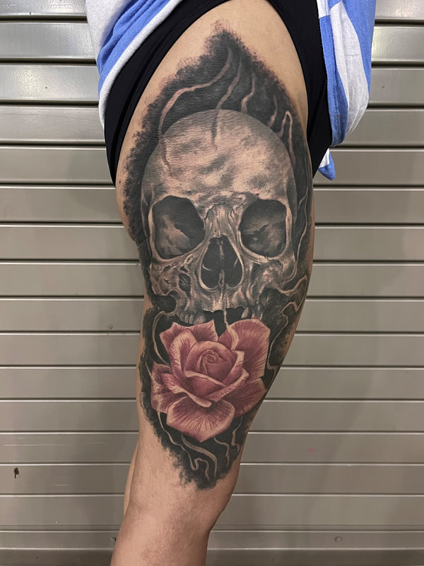 Black and grey color infused tattoo of a skull with a rose on a woman's leg.