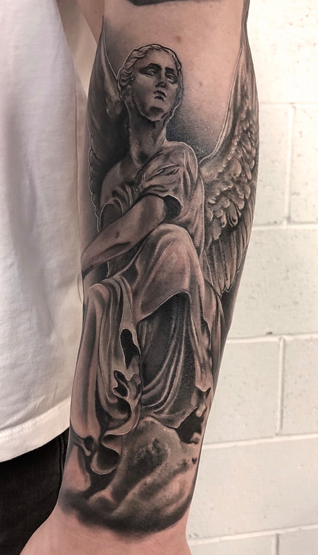 Black and grey realistic angel statue tattoo on a forearm.