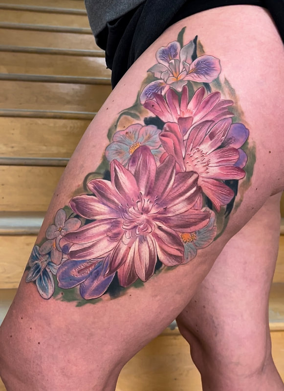 Color realism tattoo of pink, purple, and blue flowers on a woman's leg.