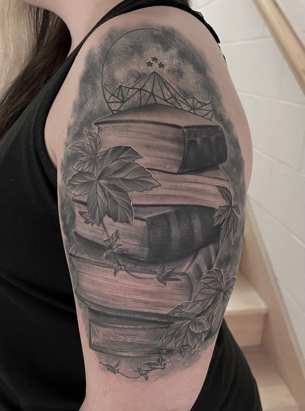 Black and grey realistic tattoo of a stack of books with ivy on an upper arm.