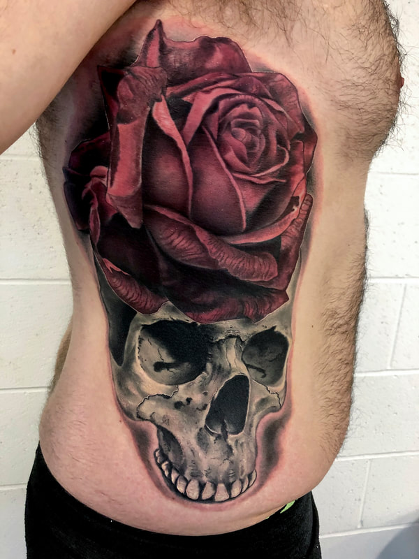 Black and grey skull tattoo with an oversized red rose on a man's ribs.