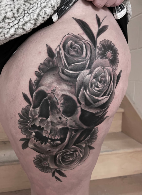 Black and grey realistic skull tattoo with roses and daisies thigh tattoo.