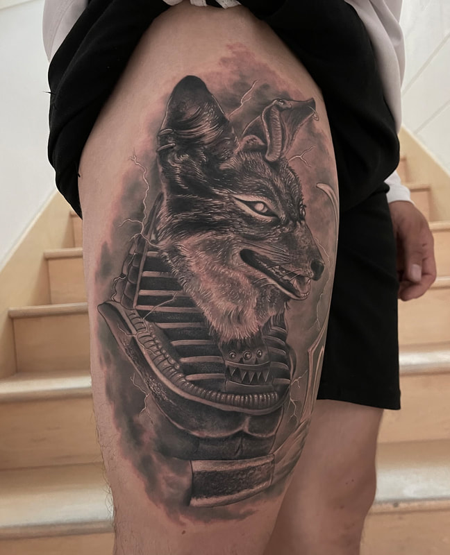 Black and grey realistic Anubis tattoo on a thigh.