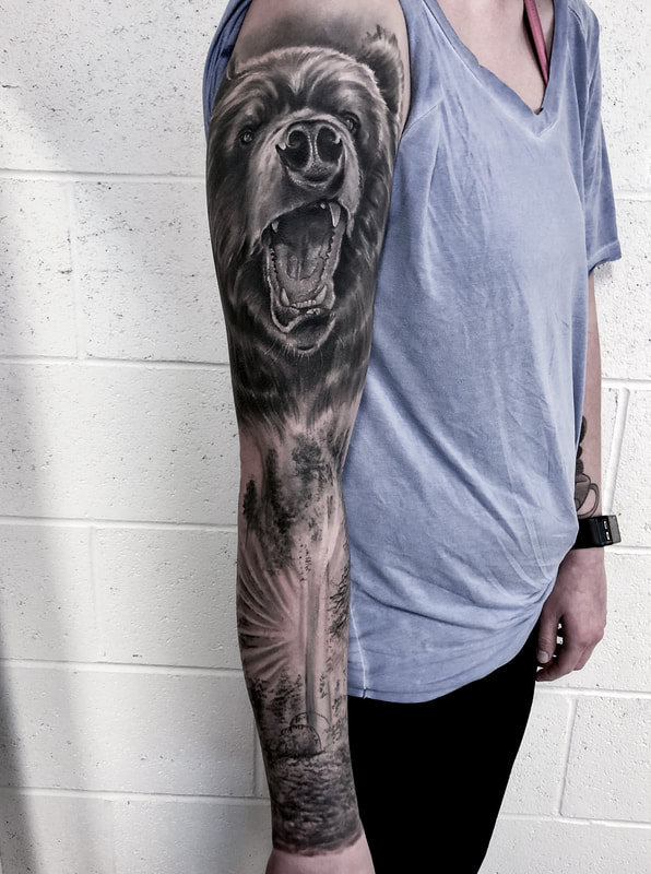Realistic black and gray sleeve tattoo of a bear and trees.