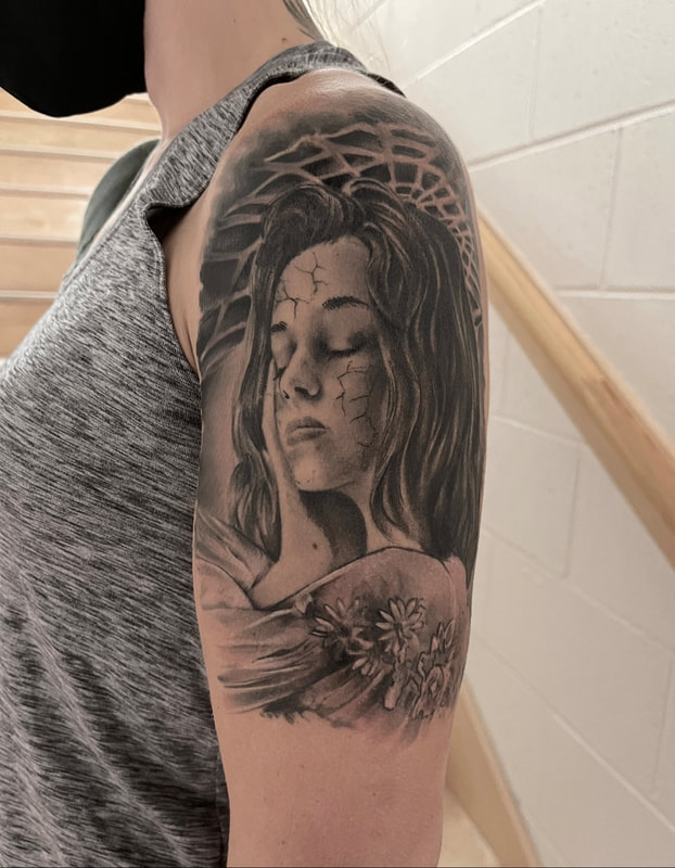 Realistic black and grey tattoo of a woman's face cracking like a statue on an upper arm.