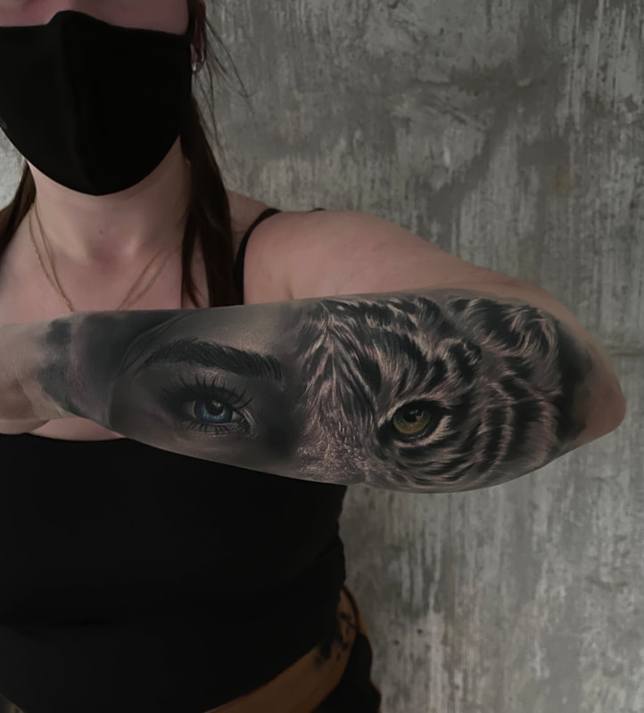 Realistic black and grey tattoo of a woman's blue eye and tiger with a yellow green eye on a woman's forearm.