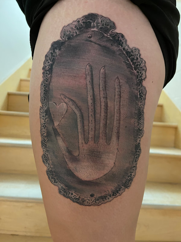 Realistic black and grey tattoo of a stitched hand holding a heart on a doily leg tattoo.