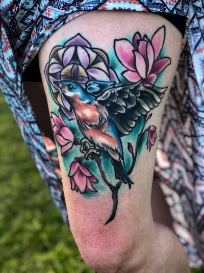 Colorful neotraditional tattoo of a blue sparrow with pink flowers on a woman's arm.