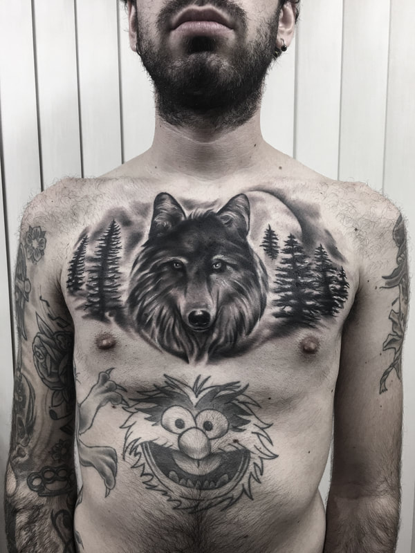 Realistic black and gray wolf chest piece tattoo with trees and a moon.
