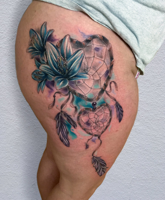 Color realism tattoo of blue lilies and heart shaped dream catcher with feathers on a woman's leg.