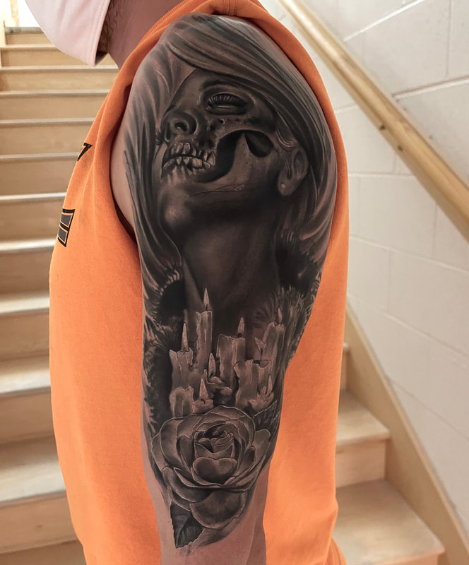 Black and grey realistic tattoo of a rose, candles, and woman with half a skull face on a man's upper arm.