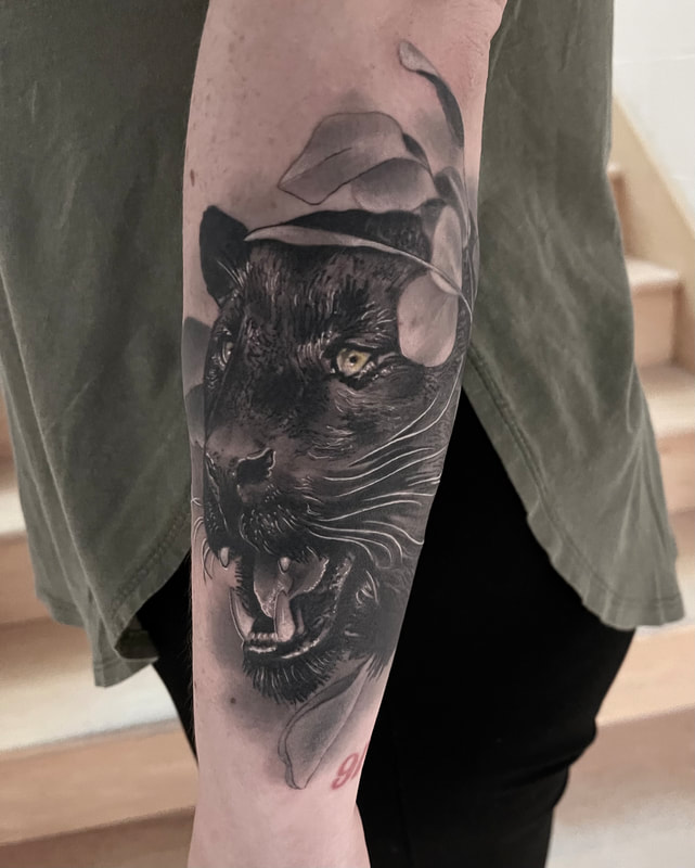 Realistic black and grey panther tattoo on a forearm.