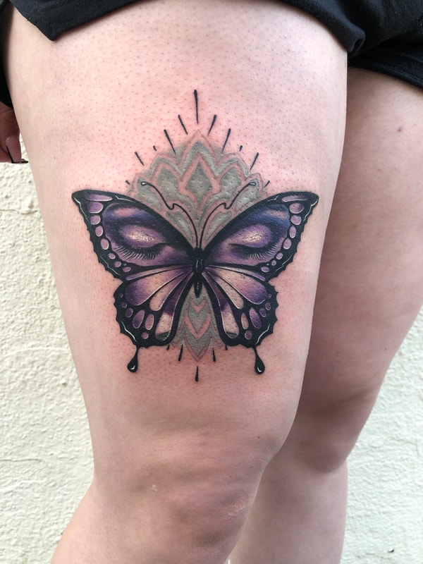 Purple butterfly with closed eyelashes tattoo above a woman's kneecap.