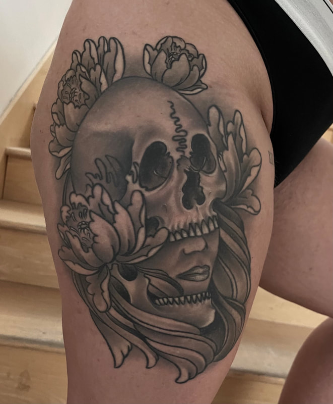 Black and gray tattoo of a Woman’s face with a skull and flowers on a thigh.