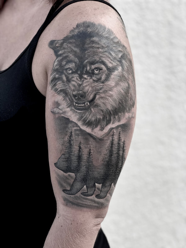 Realistic black and gray wolf with a bear and trees half sleeve tattoo.