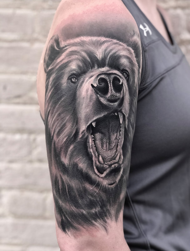 Realistic black and gray portrait half sleeve tattoo of a bear showing teeth and growling.