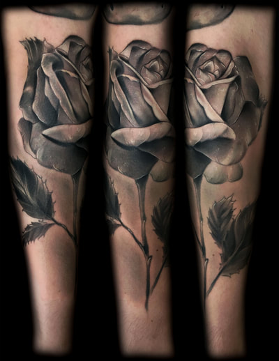 Black and gray realism tattoo of a rose on a forearm.