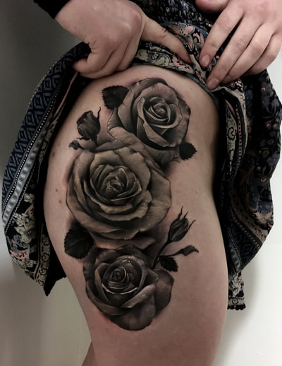 Realistic black and gray roses tattoo on a woman's thigh.