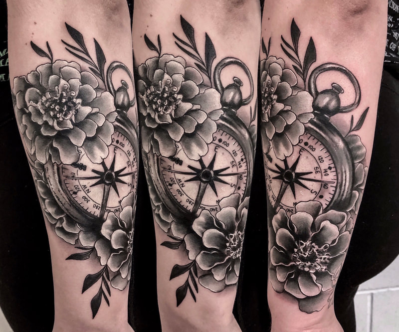Realistic black and gray tattoo of a compass and flowers on a forearm.