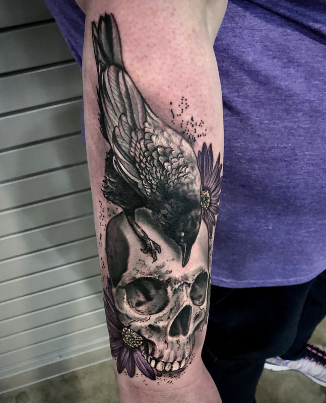 Realistic black and gray crow and skull with purple flowers tattoo on a man's forearm.