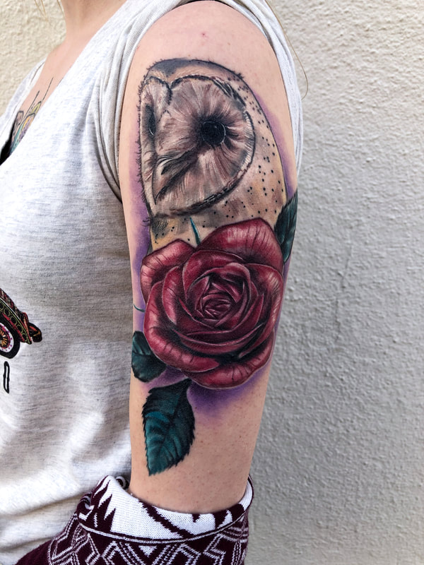 Realistic color tattoo of a barn owl with a red rose and purple lighting on a woman's arm.