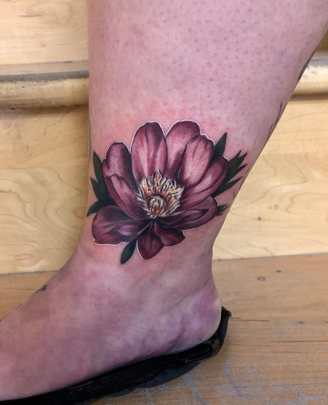 Pink realistic color tattoo of a flower on an ankle.