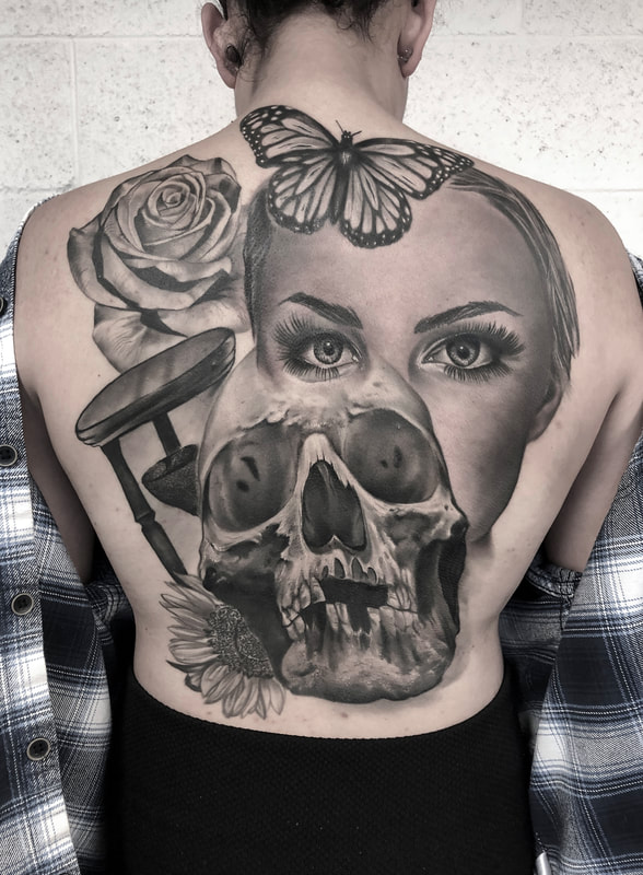 Realistic black and gray  tattoo with a woman’s face, skull, hourglass, rose, and sunflower on a woman's back.