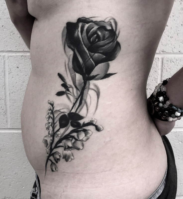 Black and grey realistic tattoo of a rose and smoke on a woman's hip and ribs.