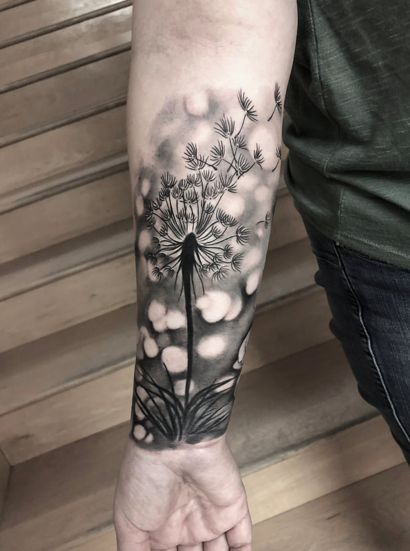 Black and grey realistic tattoo of a dandelion, Boca lights, with flying seeds on a forearm.