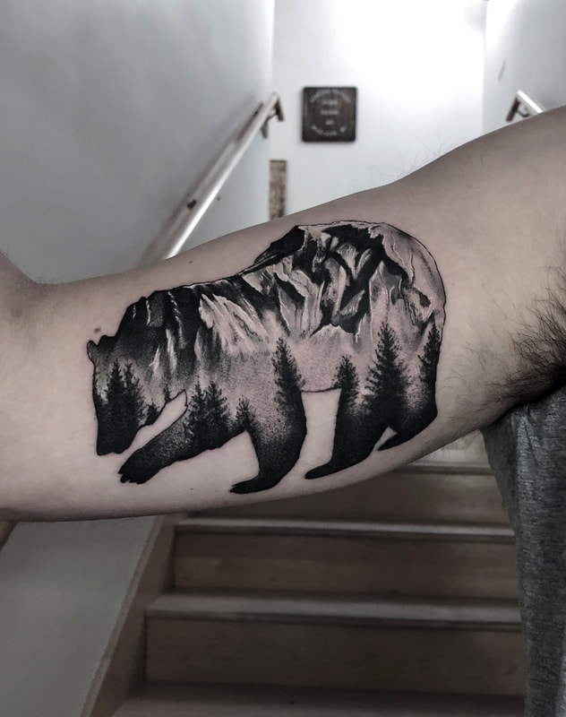 Black and grey bear outline tattoo with mountains inside on a man's inner arm.