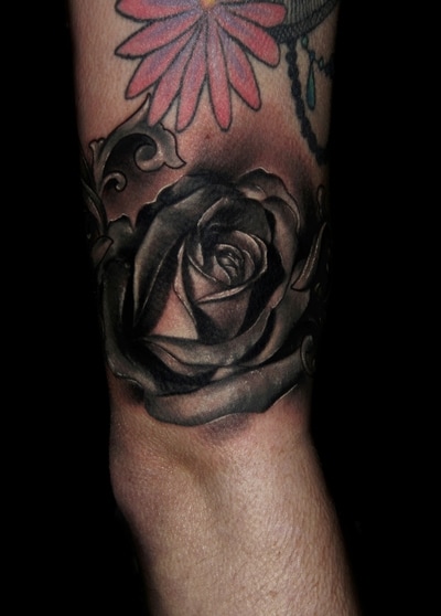 Realistic black and gray small rose with filigree on an arm.